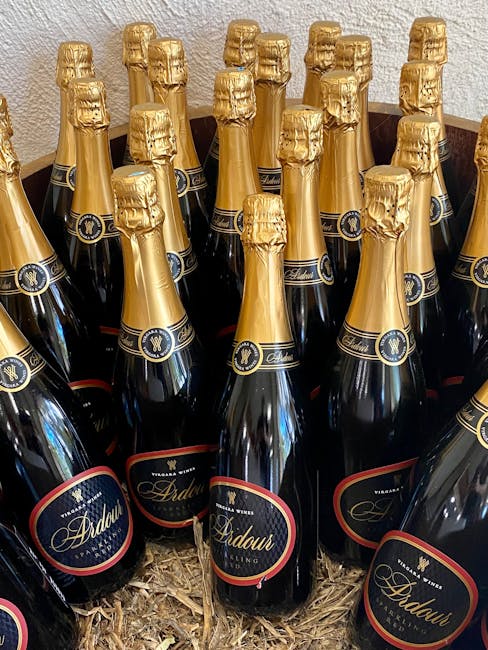 A collection of multiple dark glass bottles of Ardau sparkling wine with gold foil wrapping over the corks, arranged closely together in a container filled with wood shavings. The bottles are displayed upright on a flat surface, with their labels facing forward, showing a black, gold, and red design. The scene suggests that they are ready for transport or storage, possibly as part of packing materials during a home relocation process at a property in Maida Vale. The setting appears to be indoors with neutral-colored walls visible in the background. Occasionally, Man and Van Maida Vale’s services may involve handling such wine bottles during removals or furniture transport, ensuring careful packing and transportation, especially for delicate or valuable items like wine bottles. The image focuses solely on the bottles and packaging materials, without showing furniture or moving equipment.